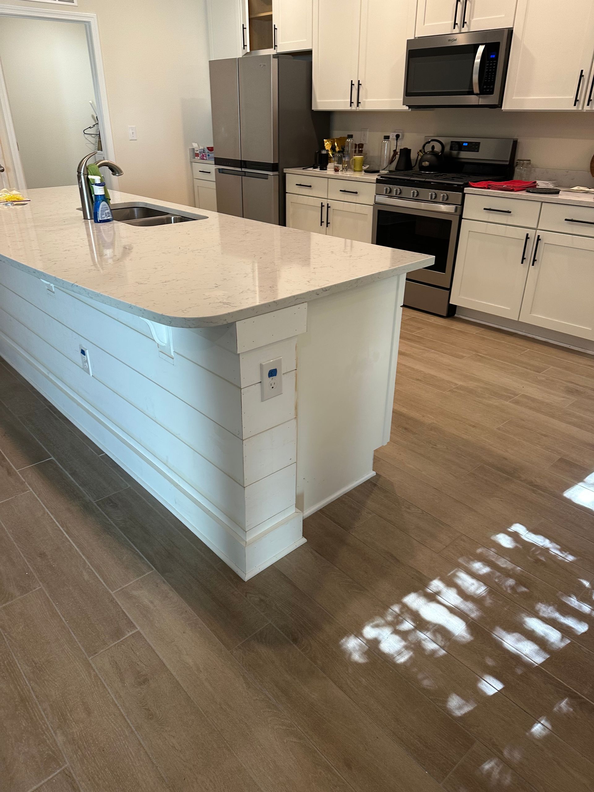 Bright modern kitchen with white island, stainless appliances, and sunlit wood floor