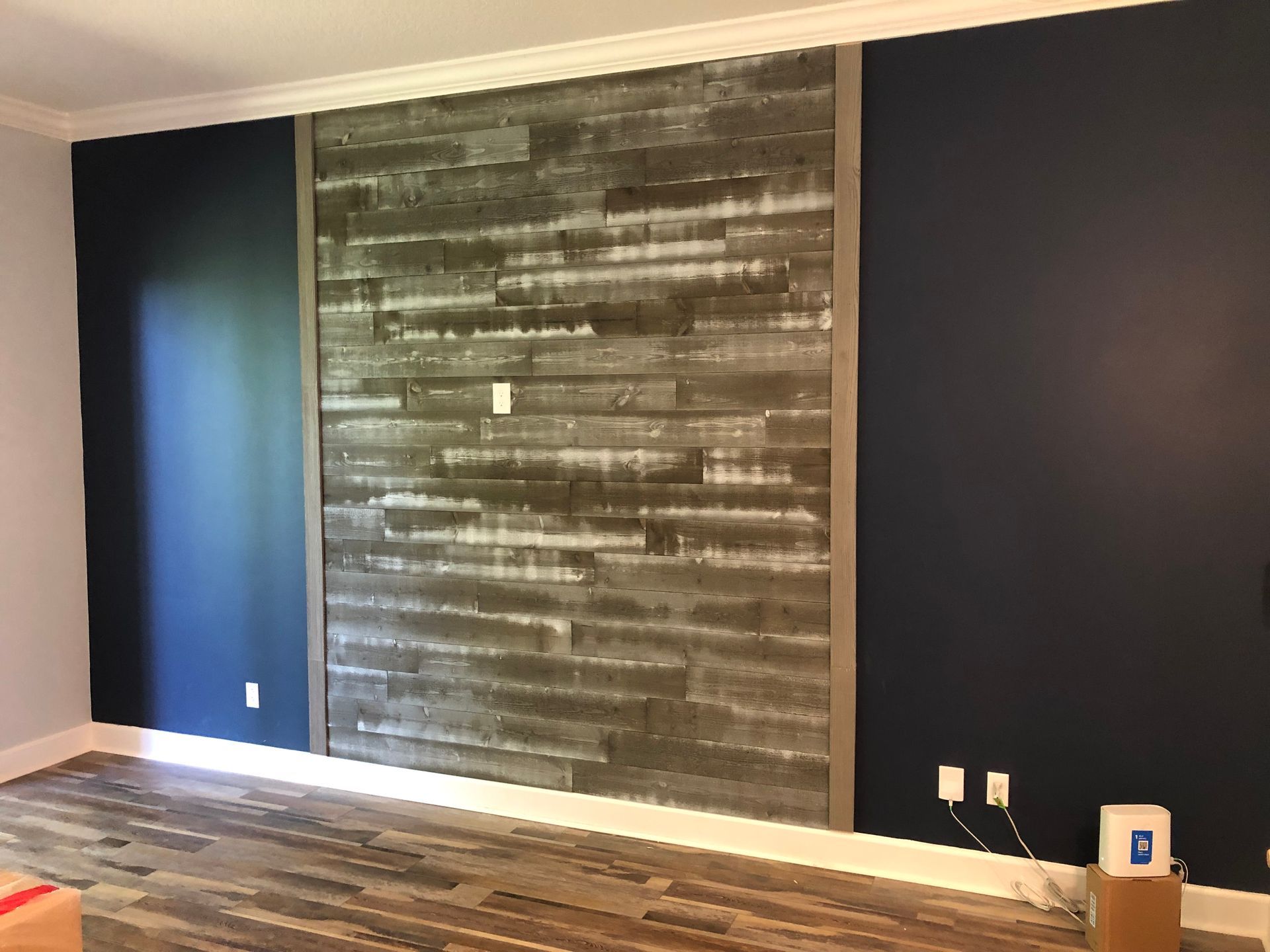 Empty room with dark blue and gray accent walls and hardwood floor, featuring a rustic wood panel focal wall.