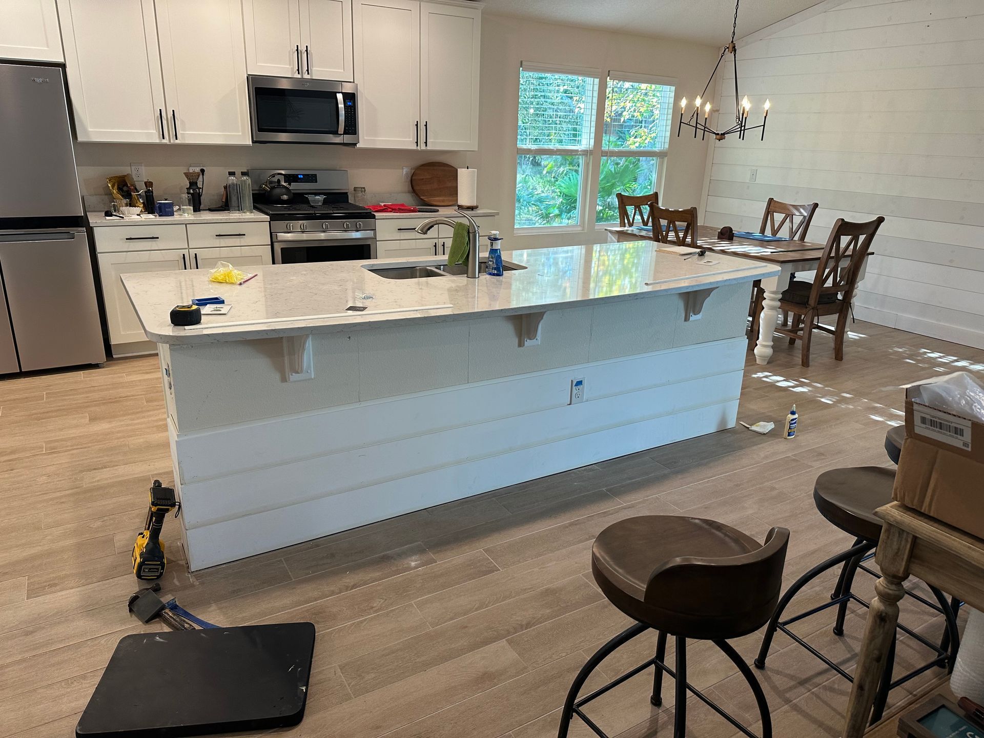 Bright kitchen with white island, light wood floor, stools, and dining table by a window