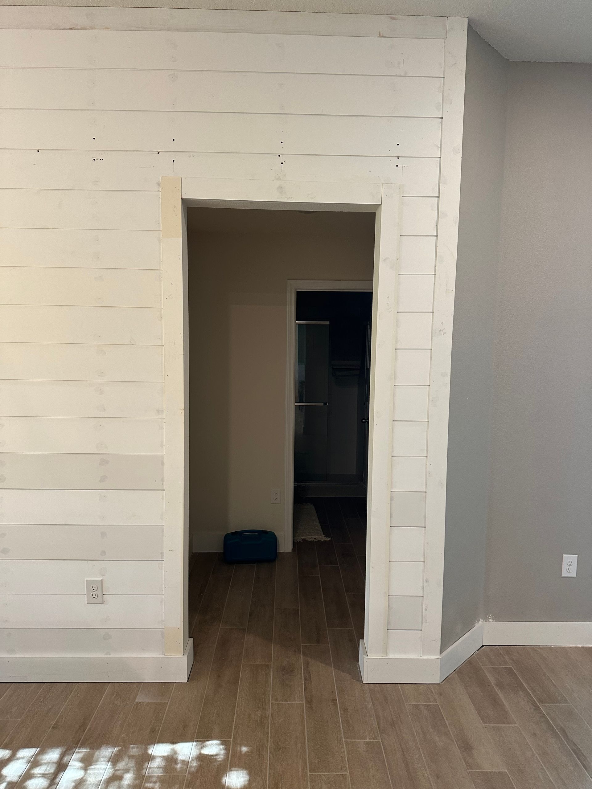 Empty room with white brick fireplace wall, doorway opening, and wood flooring under bright sunlight.
