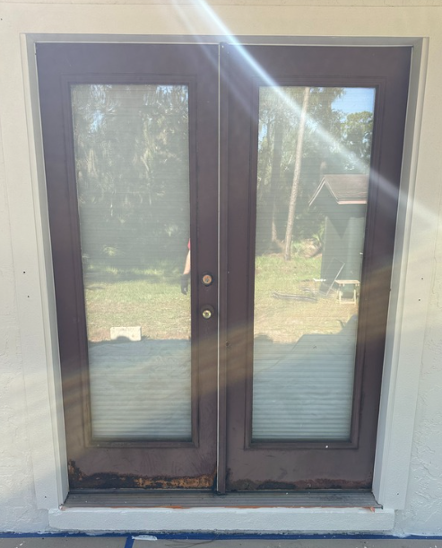 Double glass patio doors with dark brown frames and sunlight glare, viewed from outside