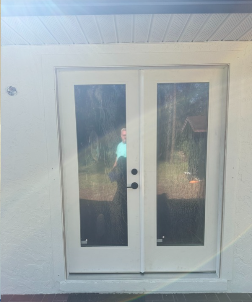 White double glass patio doors in a stucco wall, with a person faintly visible behind the left pane.