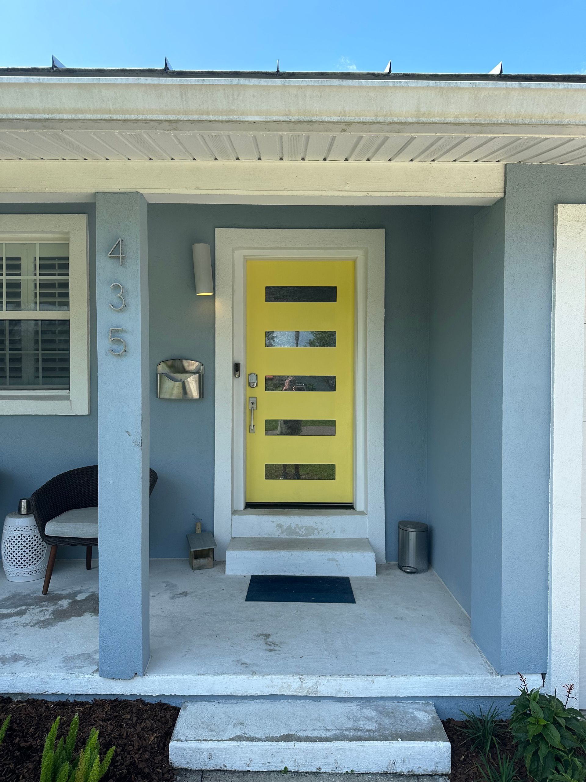 Front porch with bright yellow front door, blue walls, and steps leading up to the entrance.
