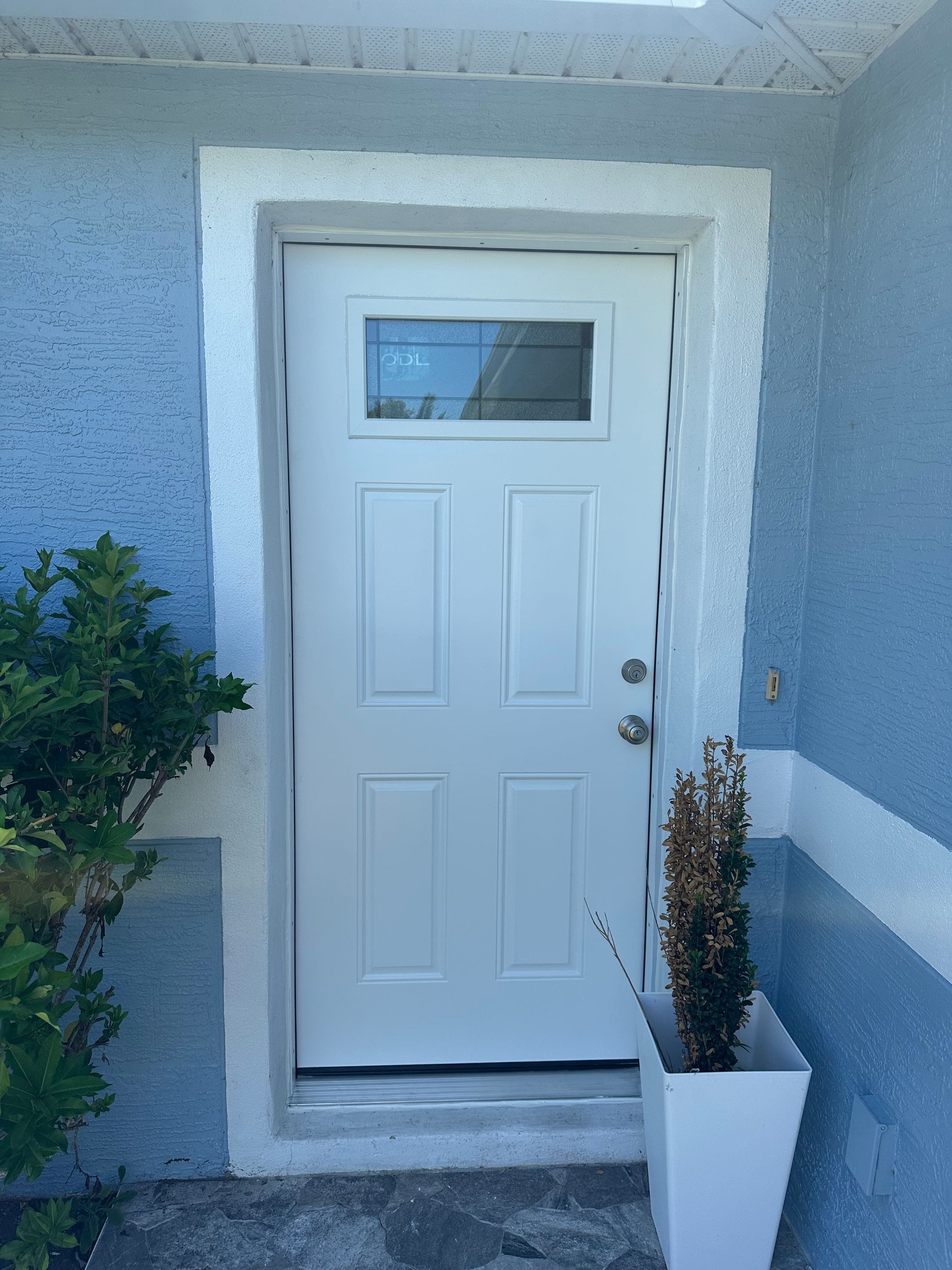 White front door with a small window, flanked by a potted plant against a light blue stucco wall.