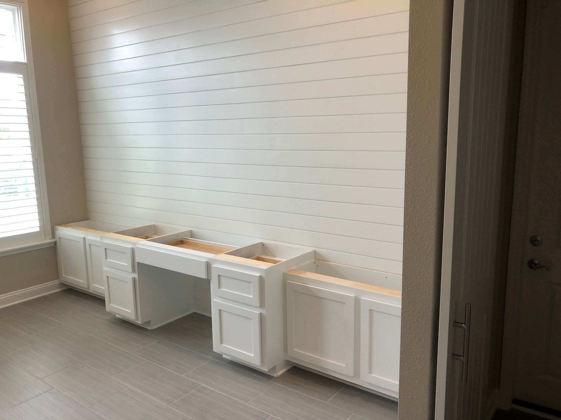 Empty room with white built-in cabinets along a shiplap wall and a large window on the left.