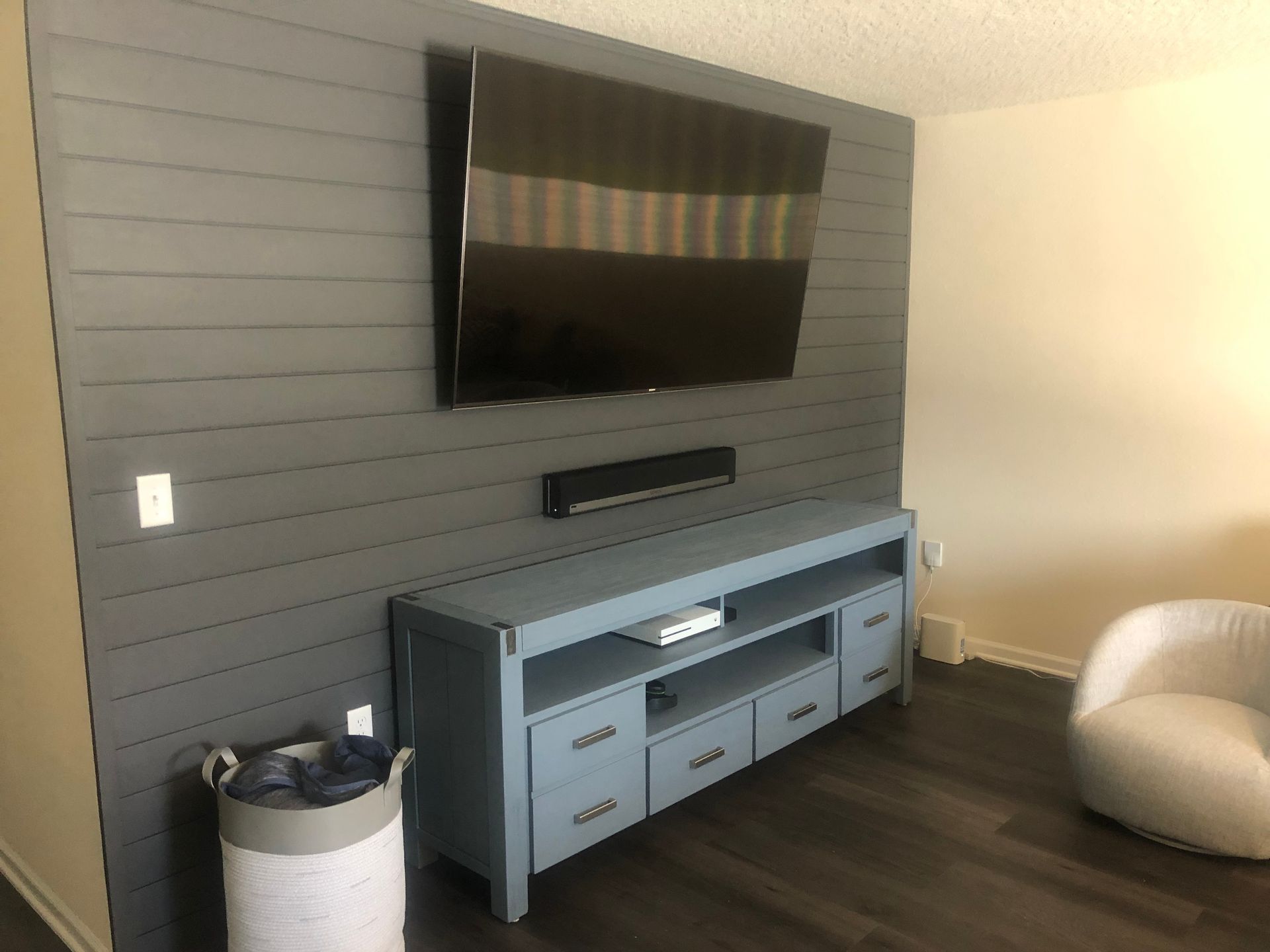 Wall-mounted TV above a blue console in a modern living room with dark accent wall and beige chair