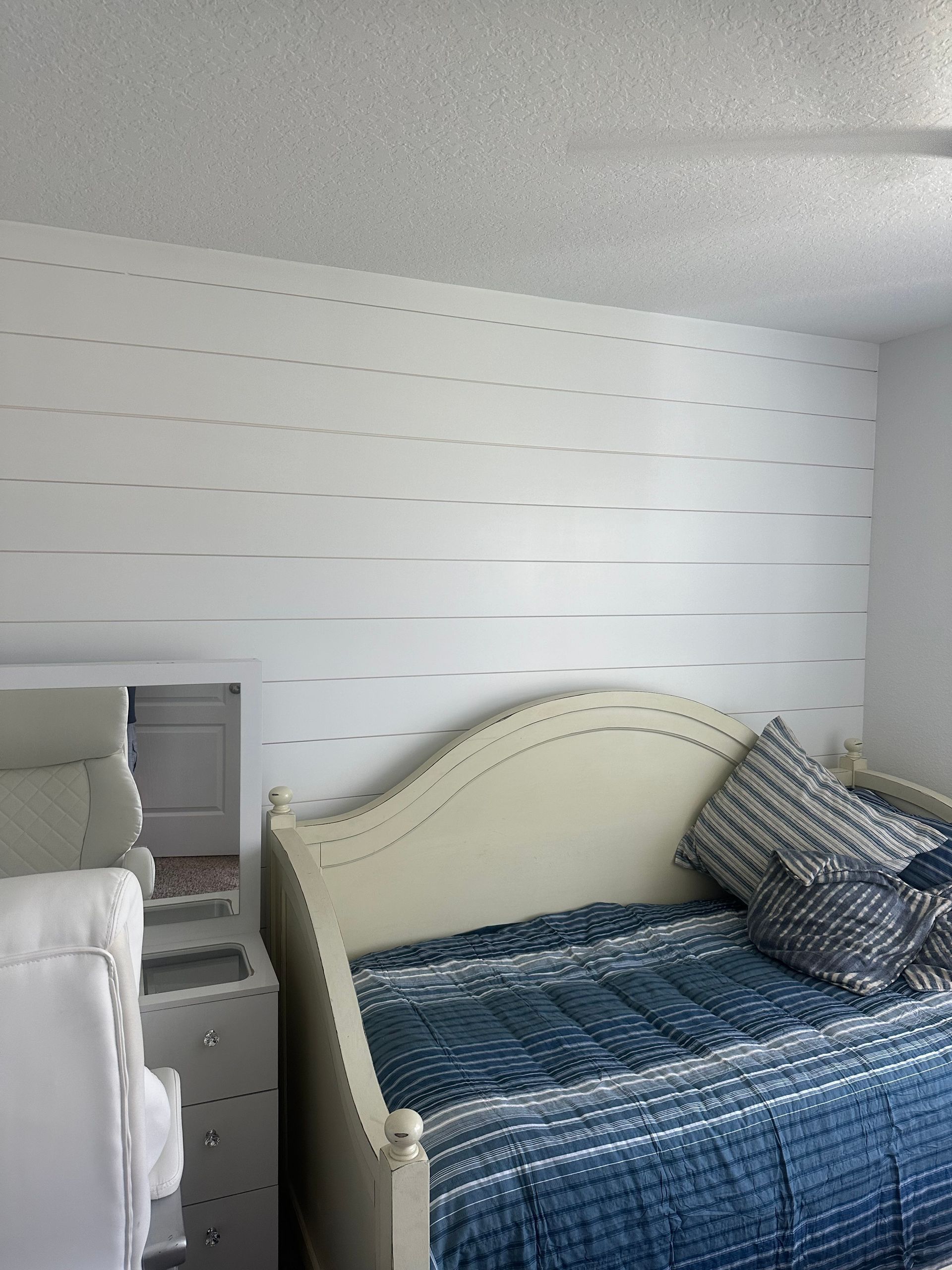 Bedroom with a white tufted daybed, blue bedding, and a striped pillow against a white paneled wall