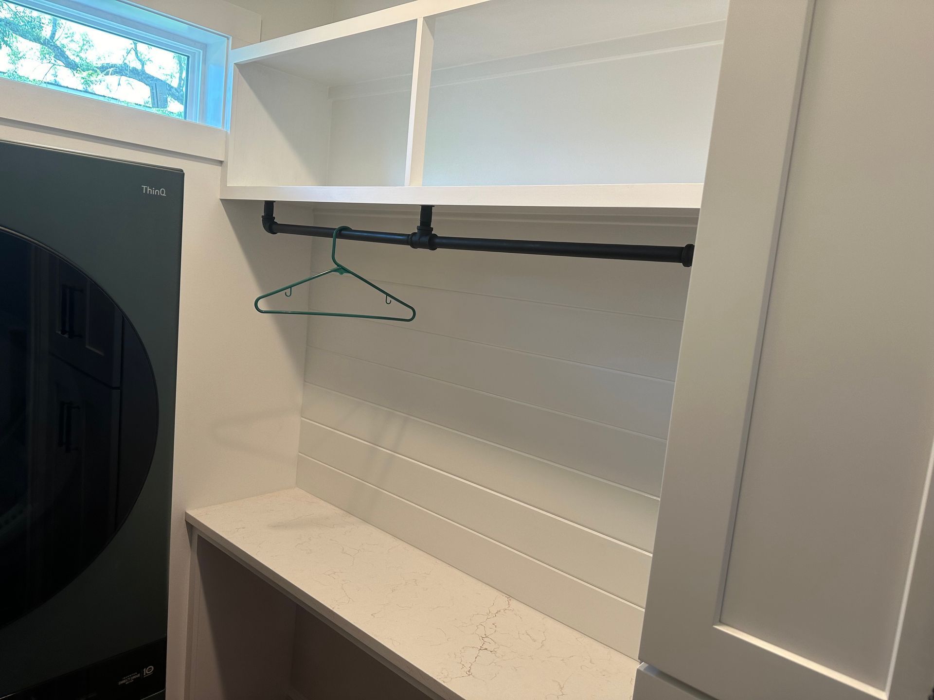 White closet with open shelving, a hanging rod, and a wire hanger beside a dark door.