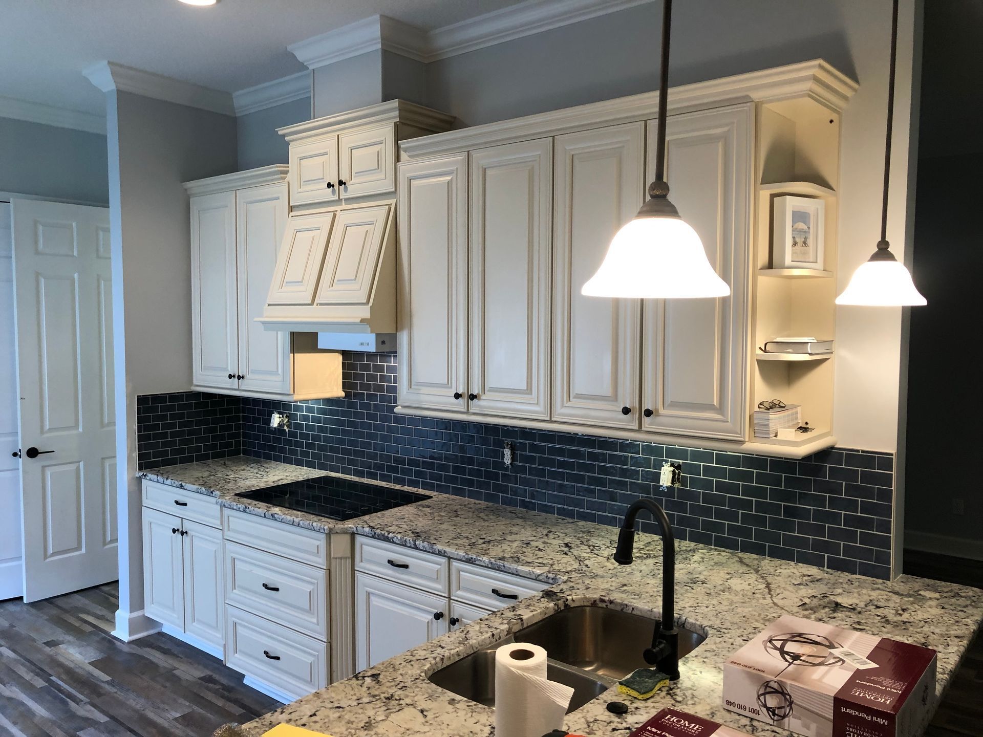 Bright kitchen with white cabinets, dark backsplash, and two pendant lights over a marble island.