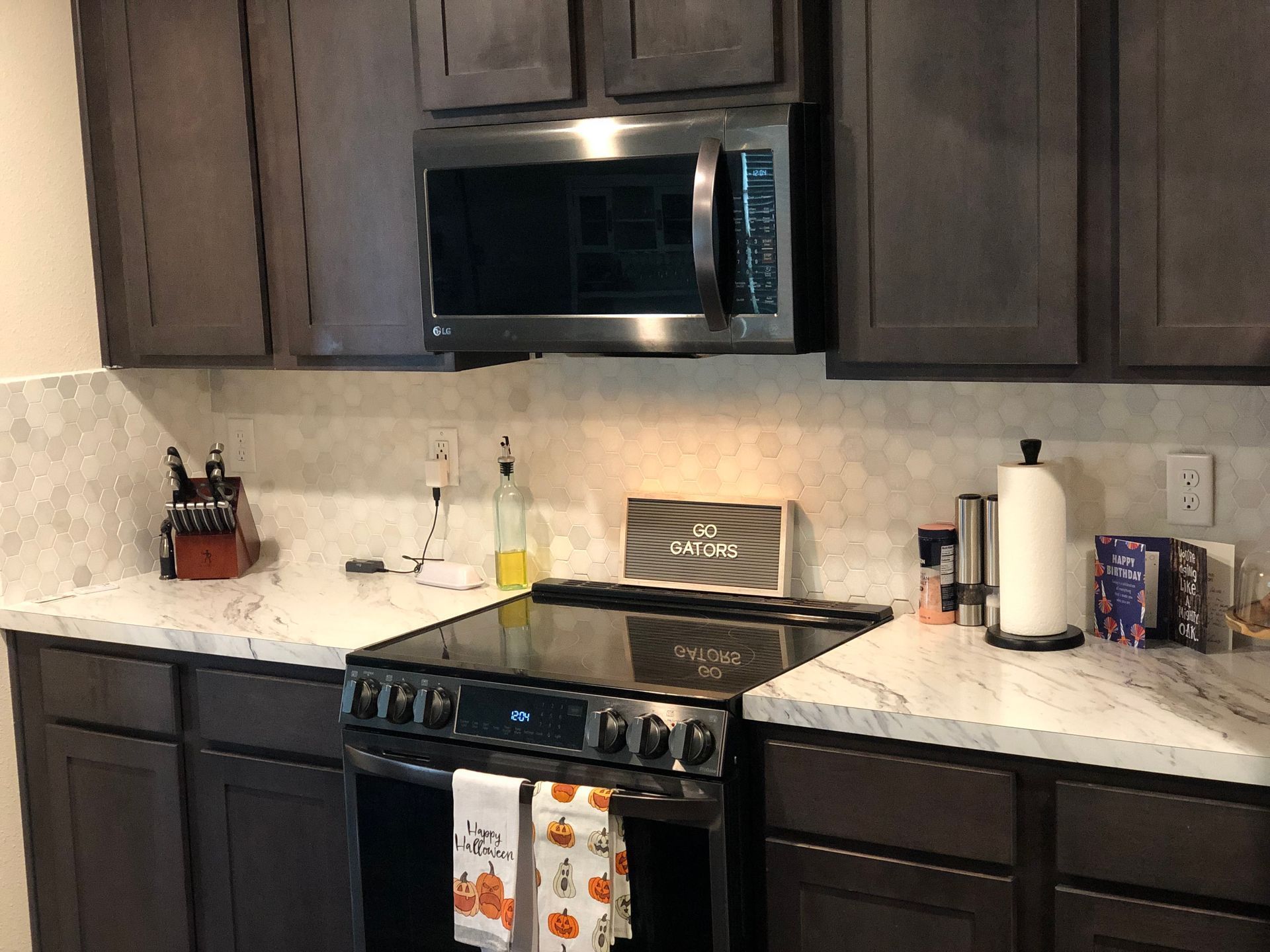 Modern kitchen with dark cabinets, stainless steel stove and microwave, and light marble backsplash