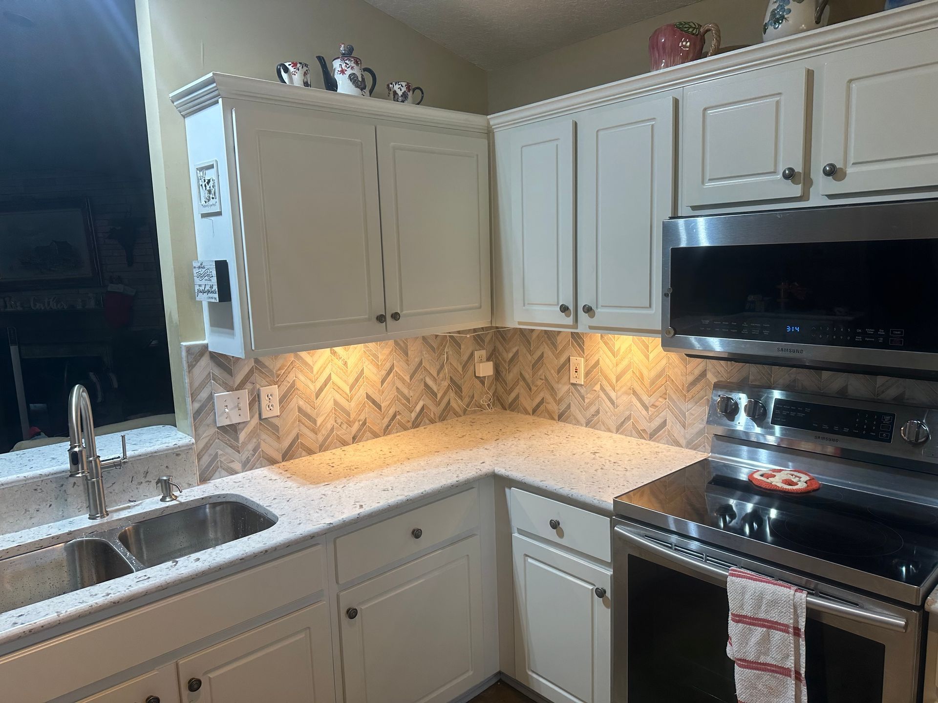Bright kitchen with beige cabinets, white countertops, stainless stove, and under-cabinet lighting.