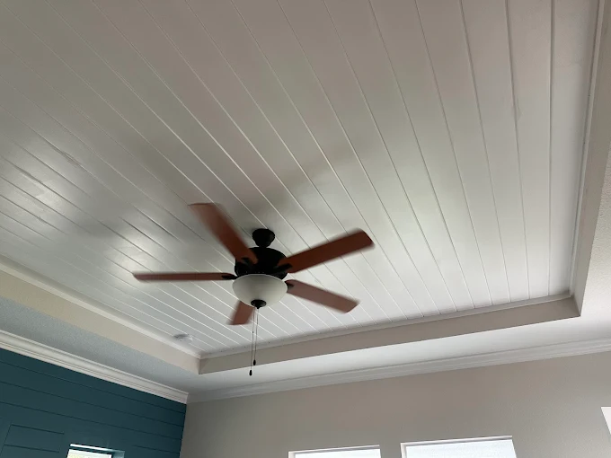 White paneled ceiling with a ceiling fan and windows in a bright room