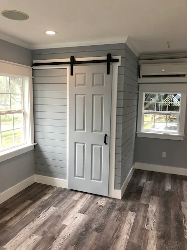 Small gray room with a white barn door, wood-look floor, windows, and a wall-mounted air conditioner.
