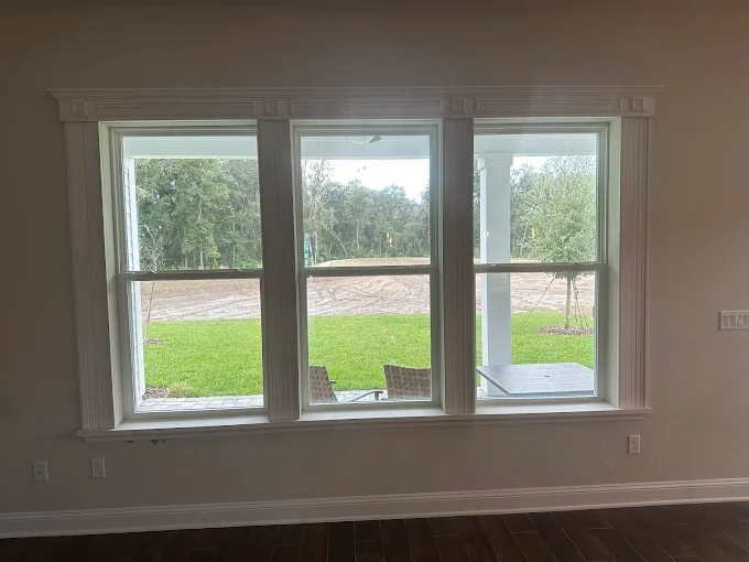 Three-pane window with white trim overlooking a green yard and trees