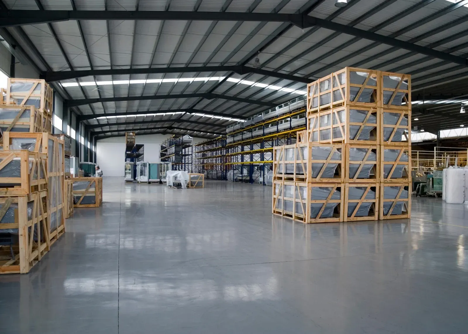 Warehouse interior with stacks of wooden crates, likely containing glass products, on a gray floor.