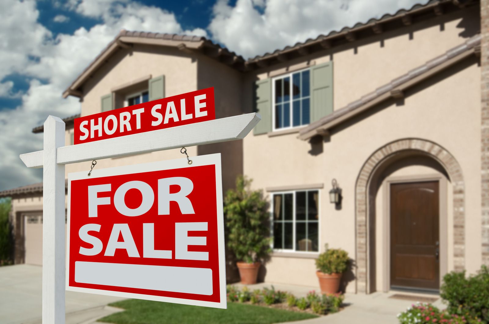 House for sale, short sale sign in front. Beige two-story home, green shutters.