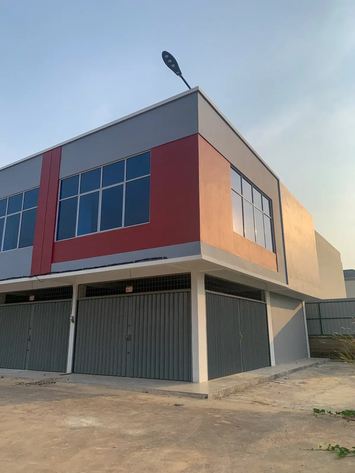 Two-story commercial building with gray and red facade, gray garage doors, and large windows.