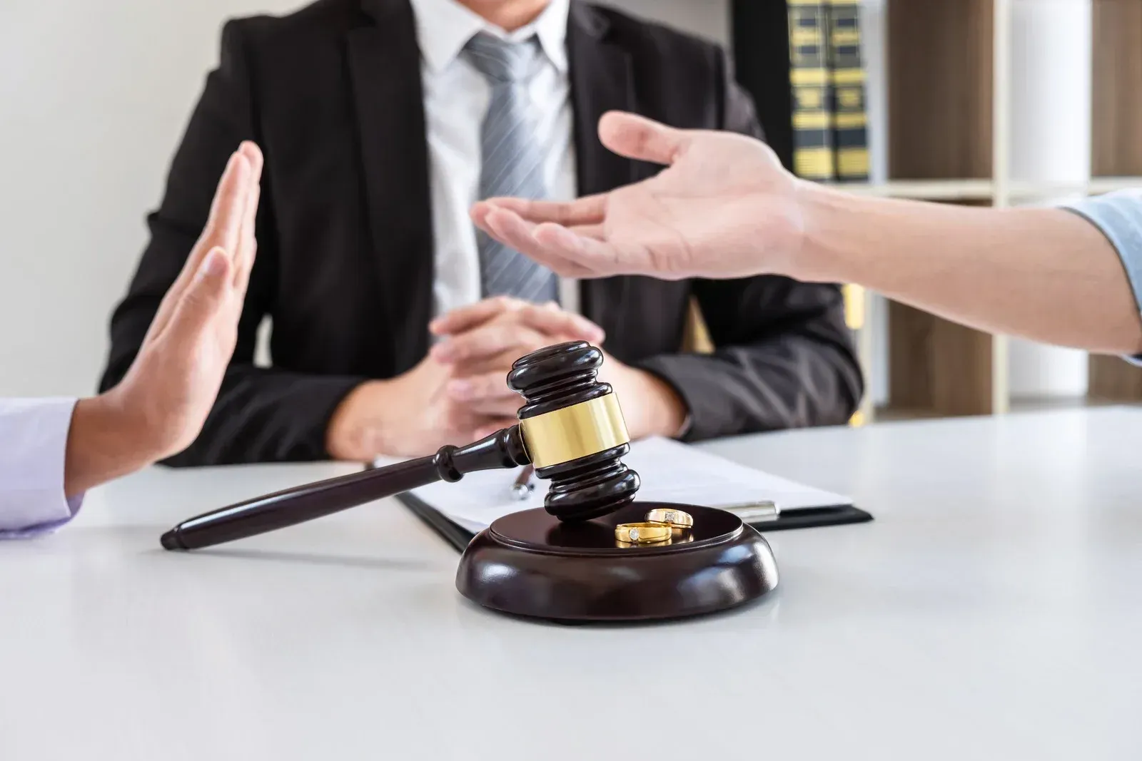 Divorce proceedings: Judge with gavel, people with hands raised, wedding ring.