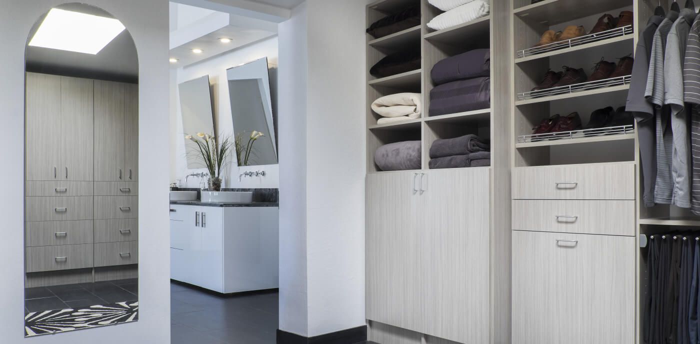 A walk in closet with a bathroom in the background