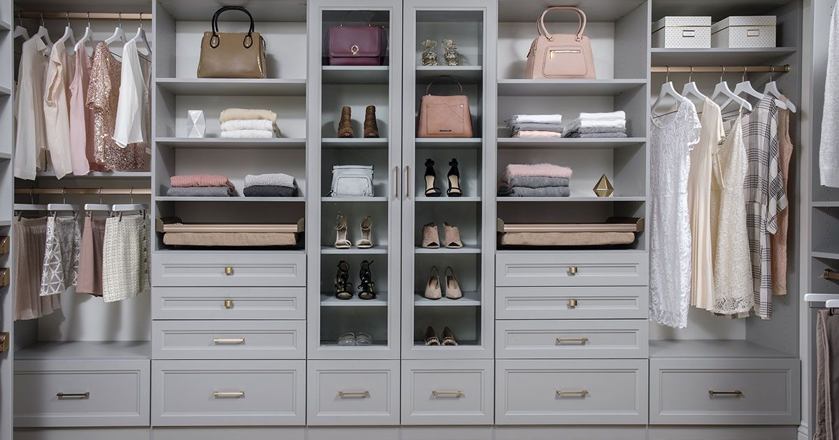 Walk-in closet with shelves, drawers, and hanging rods filled with clothing, shoes, and accessories; neutral tones.