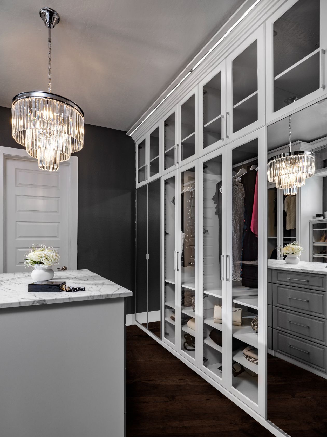 A walk in closet with glass doors and a chandelier hanging from the ceiling.