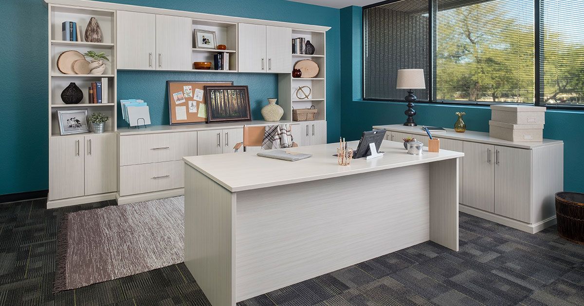 White office with teal walls, desk, cabinets, decor, and window with outdoor view.