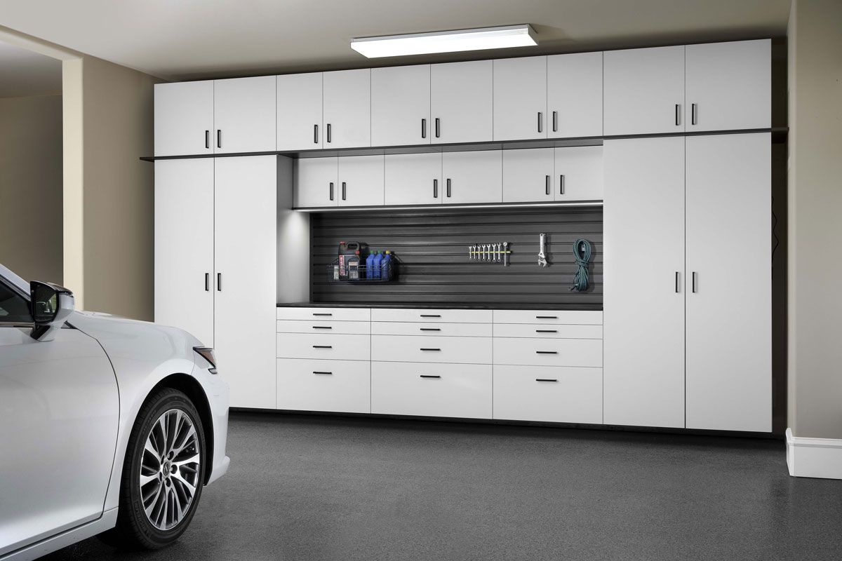 a white car is parked in a garage with white cabinets .