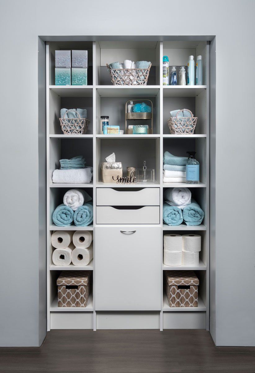 a bathroom closet filled with towels , toilet paper , baskets , and a drawer .