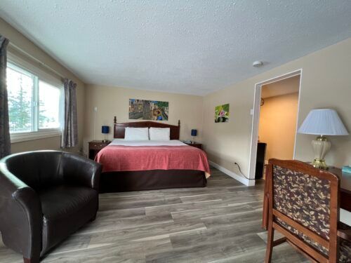 A hotel room with a king size bed , chair , desk and lamp.