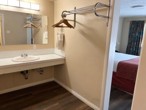 A bathroom in a hotel room with a sink , mirror and clothes rack.