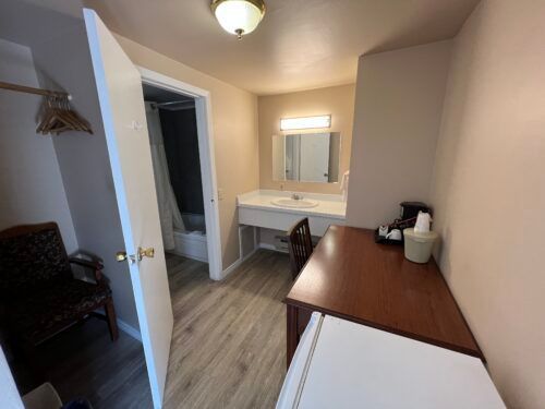 A hotel room with a desk , chair , sink and mirror.