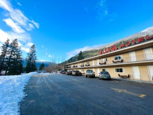 A motel with cars parked in front of it in the snow.