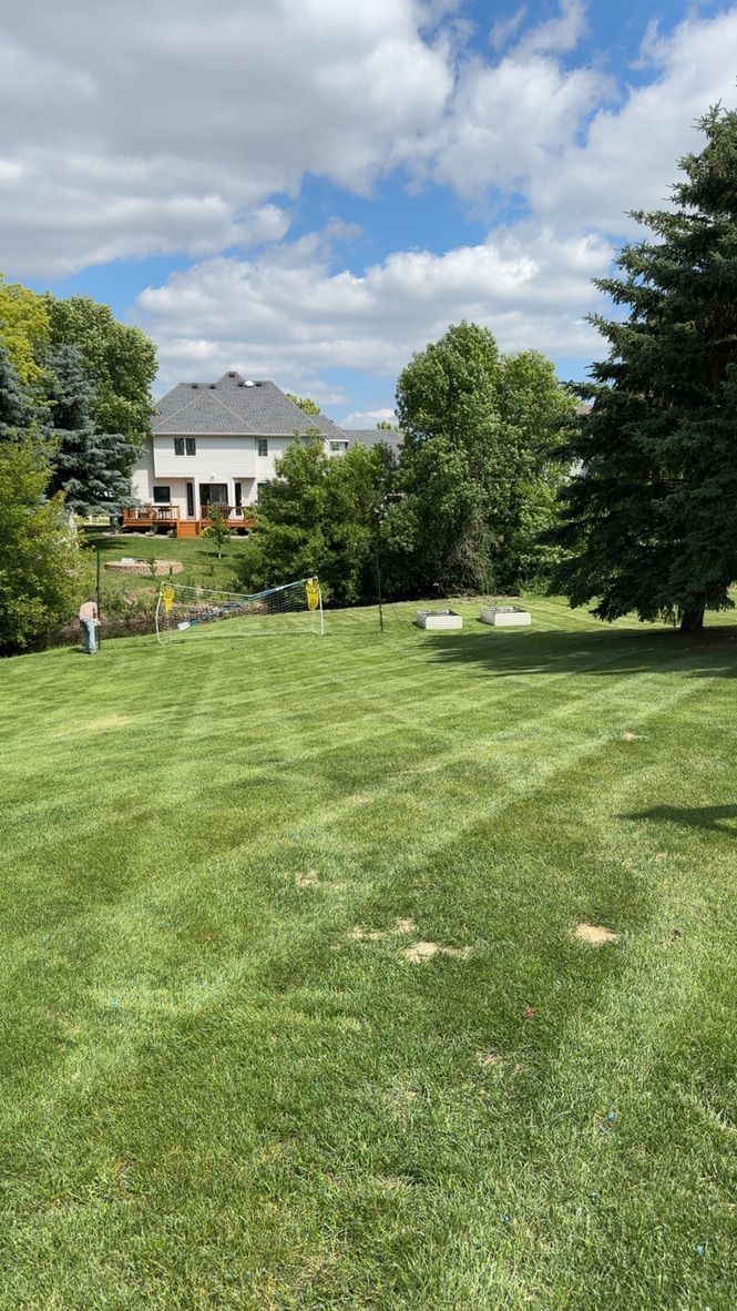 Grassy park with a few trees, a large house in the background, and a partly cloudy sky