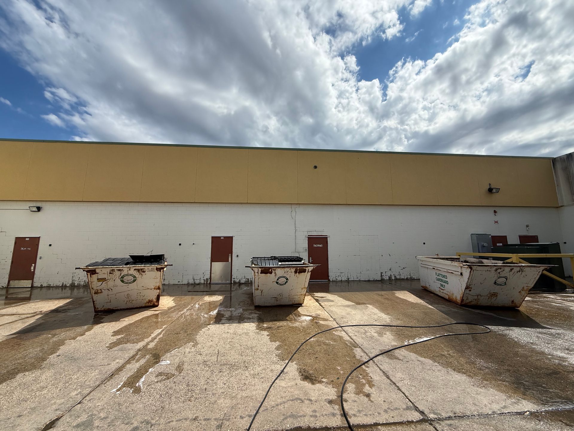 Industrial rooftop with three large dumpsters, red doors, and a cloudy sky.
