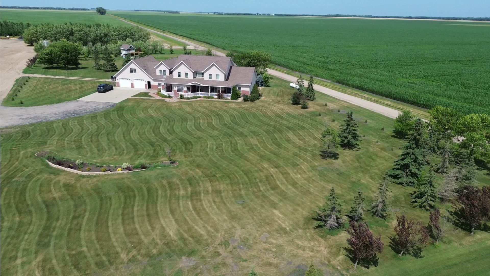 Aerial view of a farmhouse with a large mowed lawn beside green fields and a dirt road.