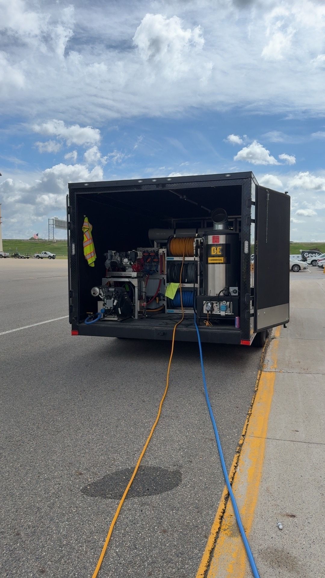 Open utility trailer with equipment inside, parked on a road under a cloudy sky.