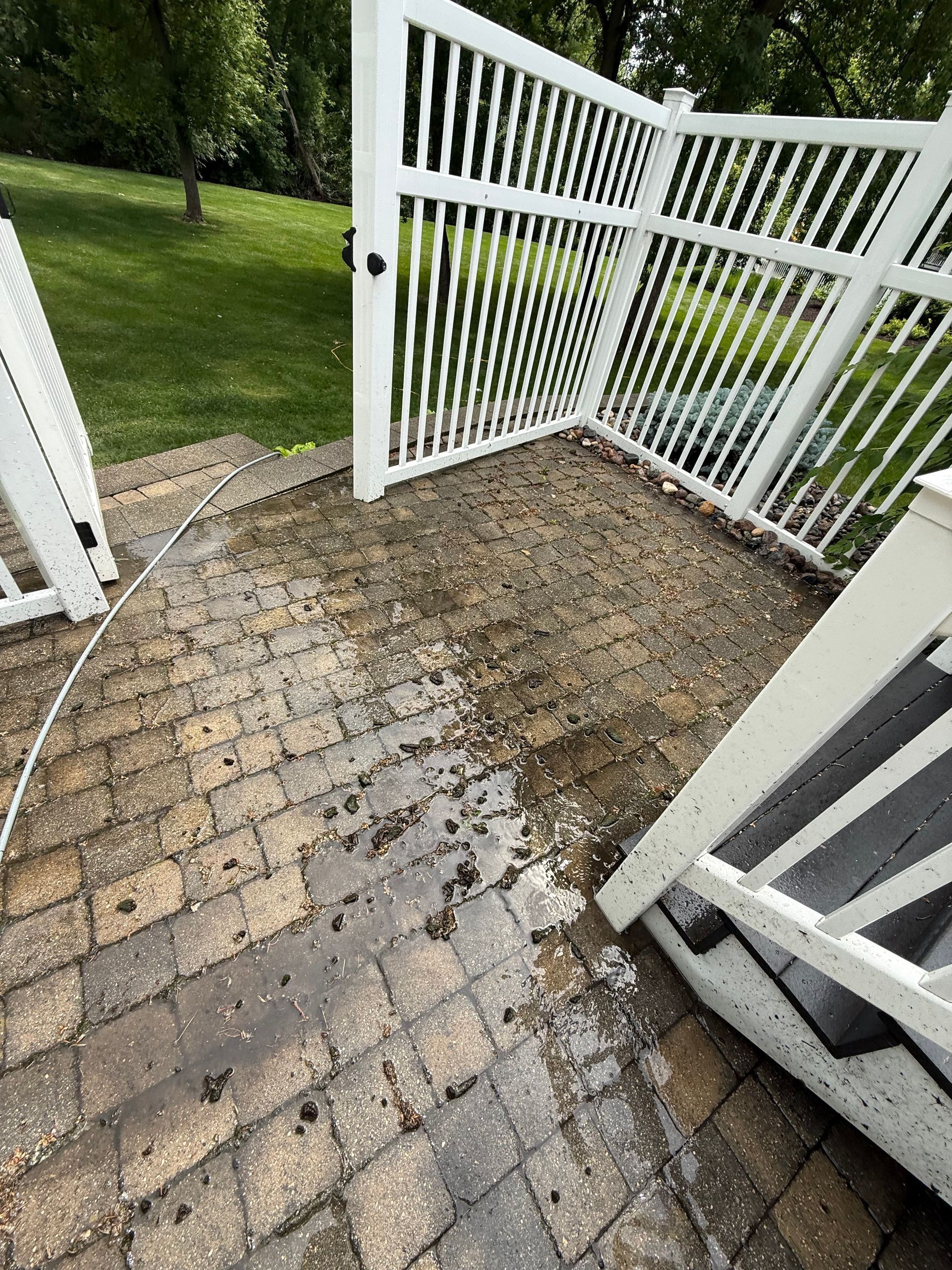 Wet brick patio with open white gate leading to a grassy yard