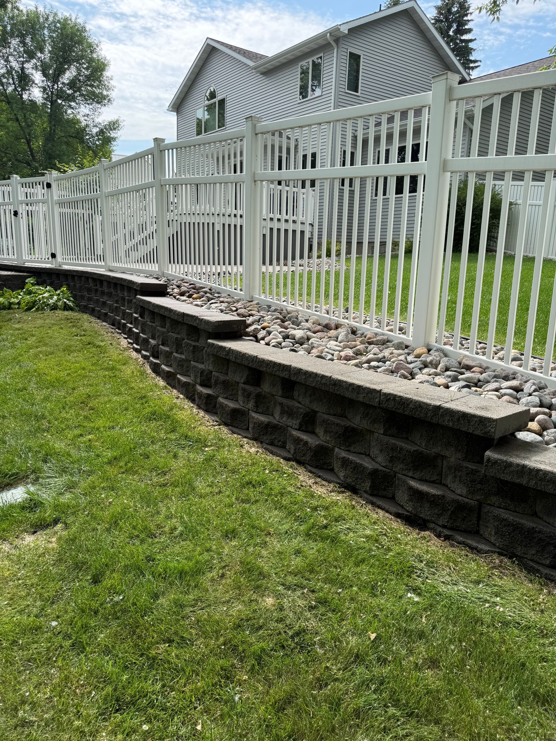 White house with a long white fence above a stone retaining wall on a grassy slope