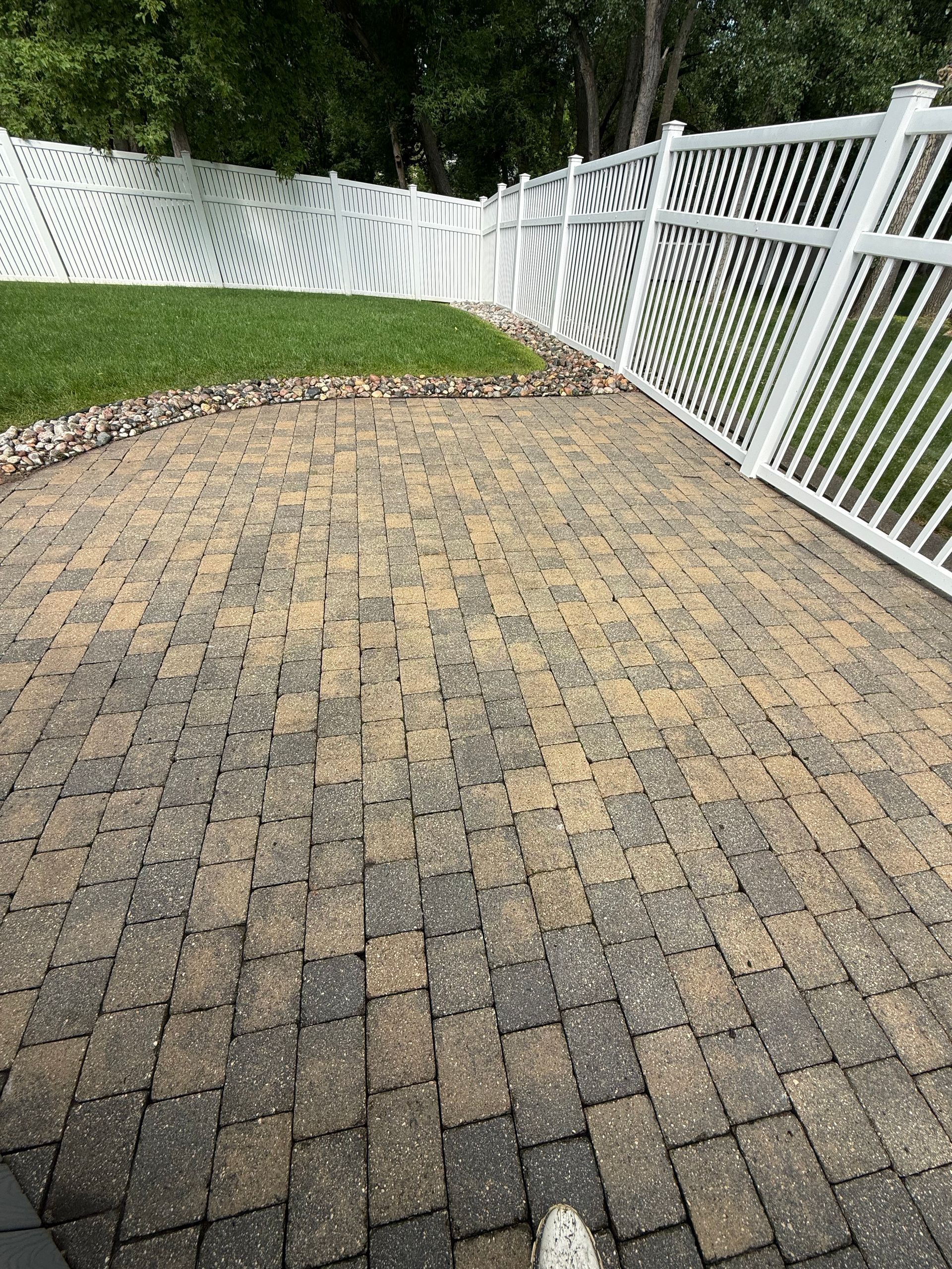 Curved brick patio bordered by white vinyl fence and green lawn after rain