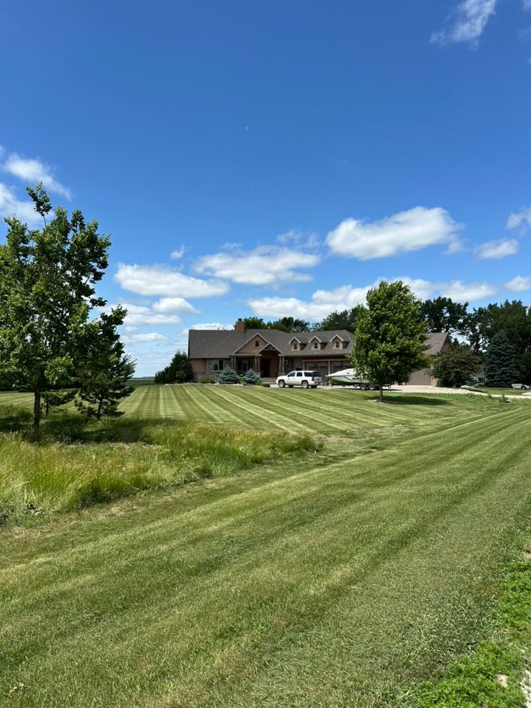 Mowed grassy field leading to a brick building under a bright blue sky with scattered clouds