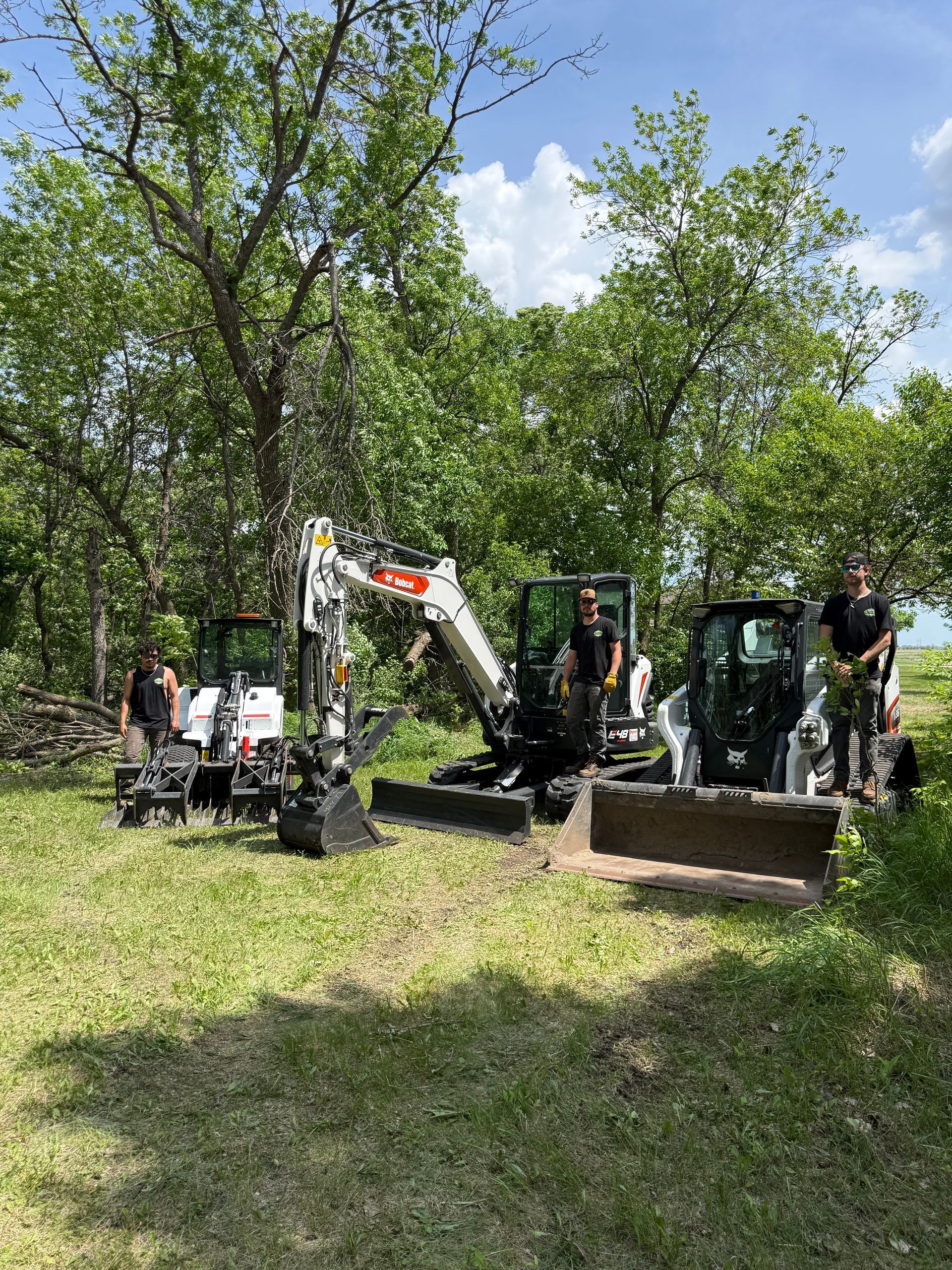 Workers with excavator and tractor in a wooded area clearing brush and moving dirt.