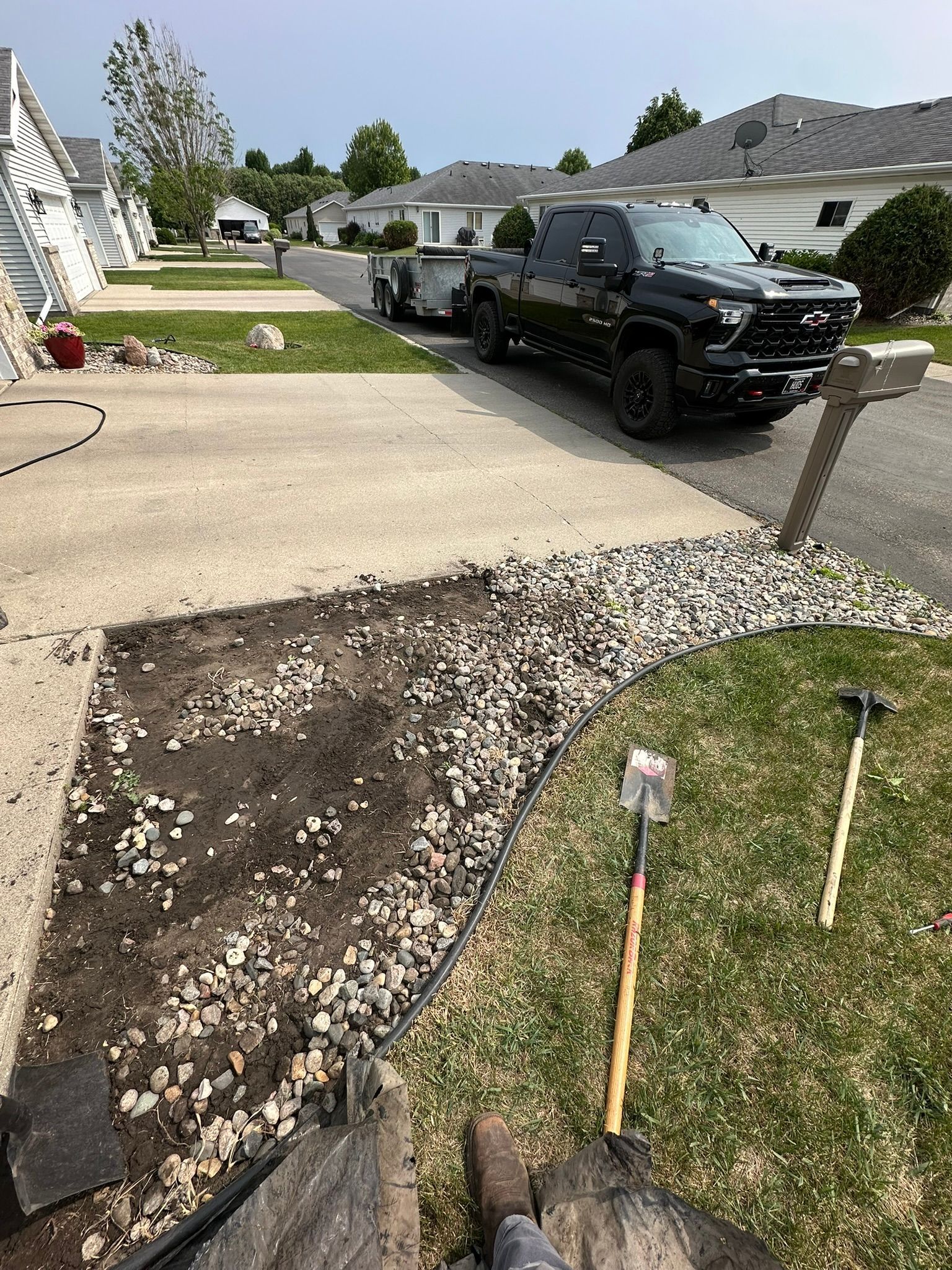 Driveway repair area beside a black pickup truck in a suburban neighborhood, with exposed dirt and gravel.