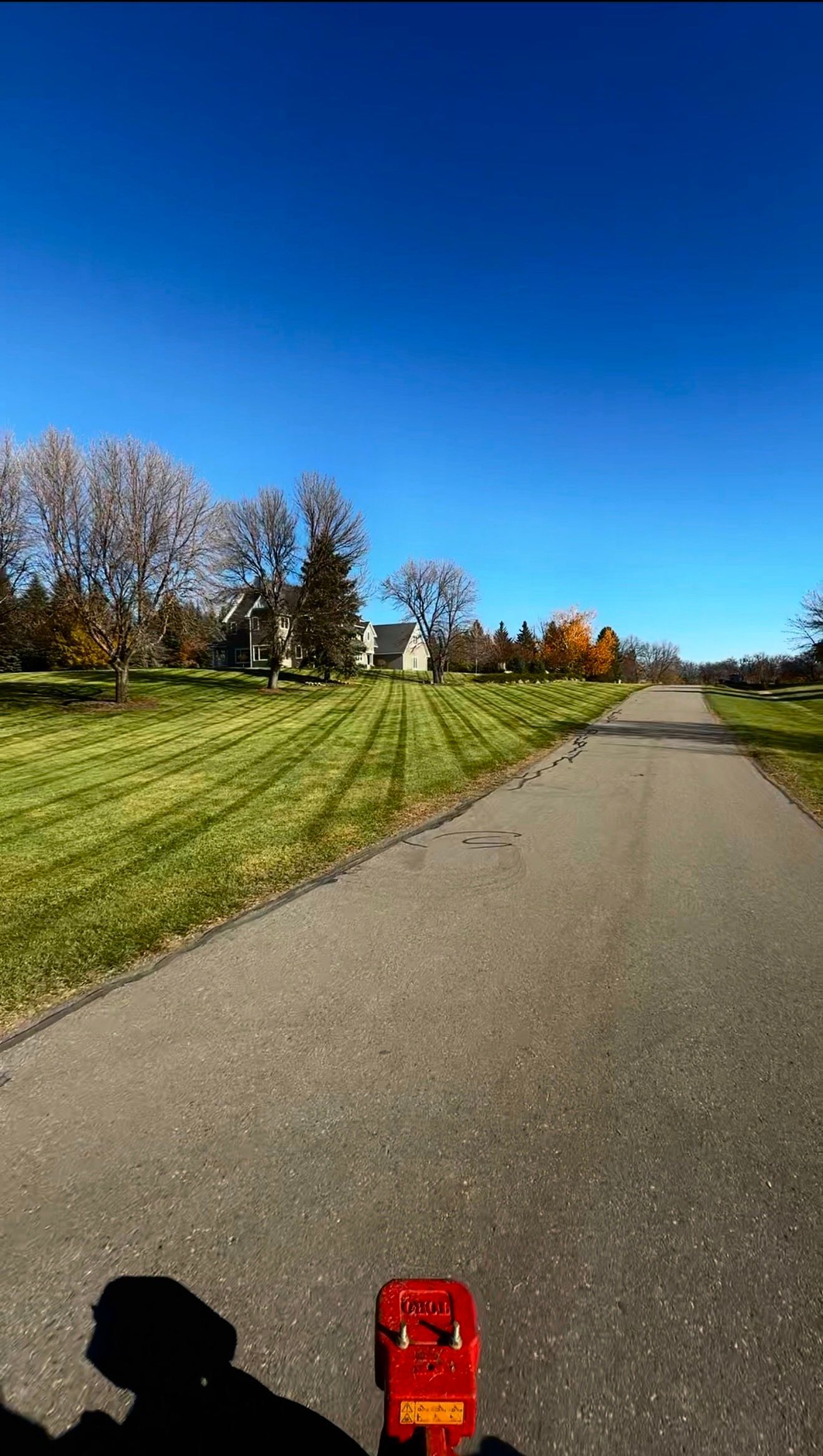 Sunny park path beside grassy hill and autumn trees, with a small red toy at the bottom of the frame