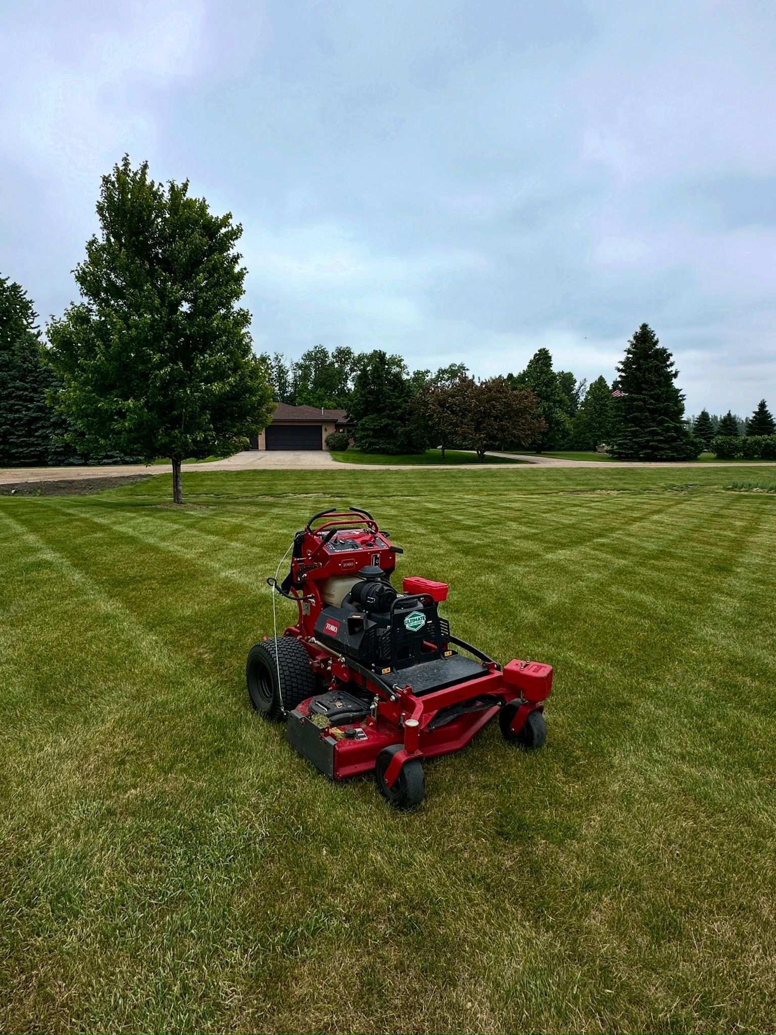 Red lawn mower on a grassy field near trees under a cloudy sky