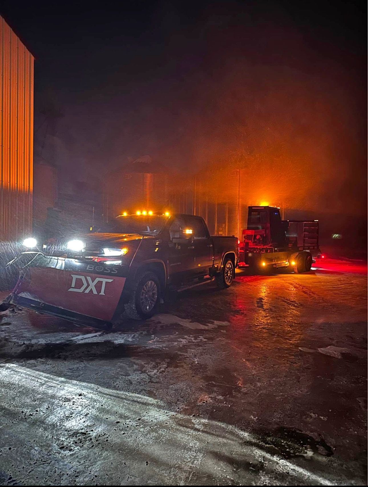 Two tow trucks with flashing lights on a smoky, icy road at night