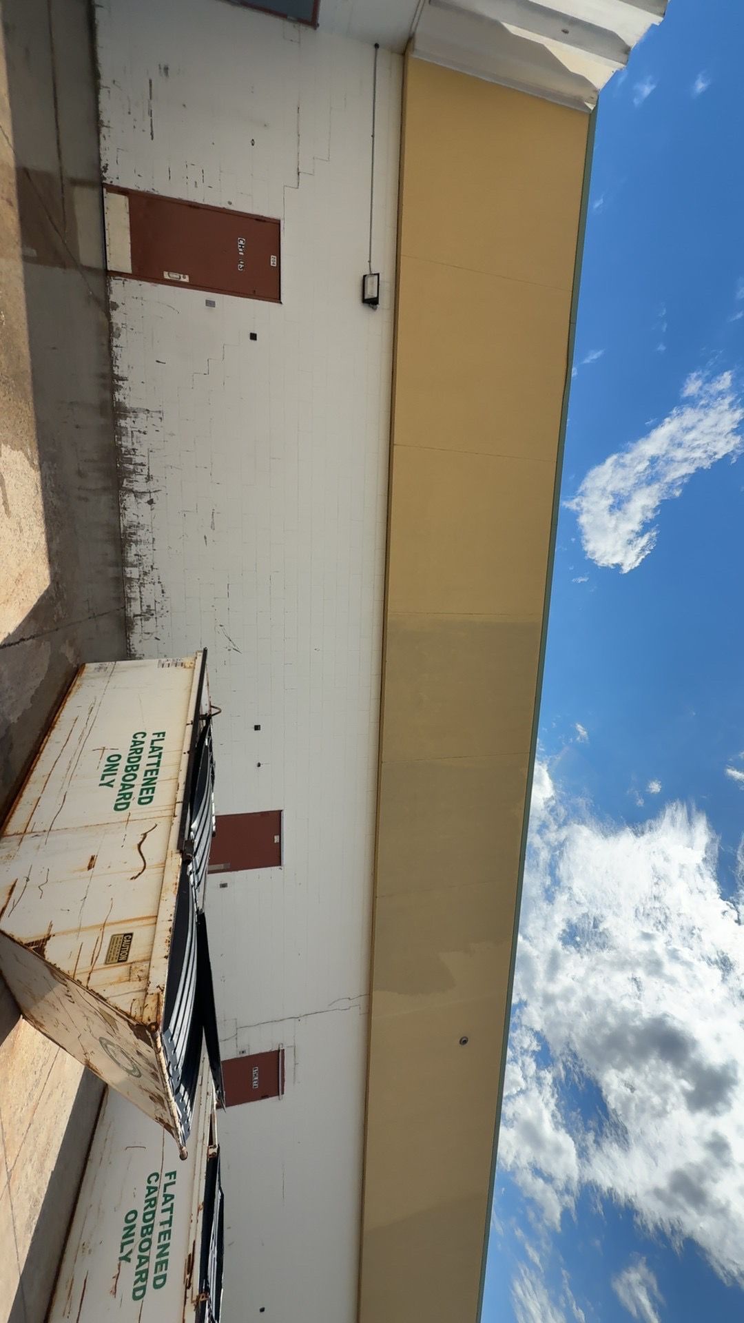 White industrial building with red doors and stacked boxes under a blue sky with clouds