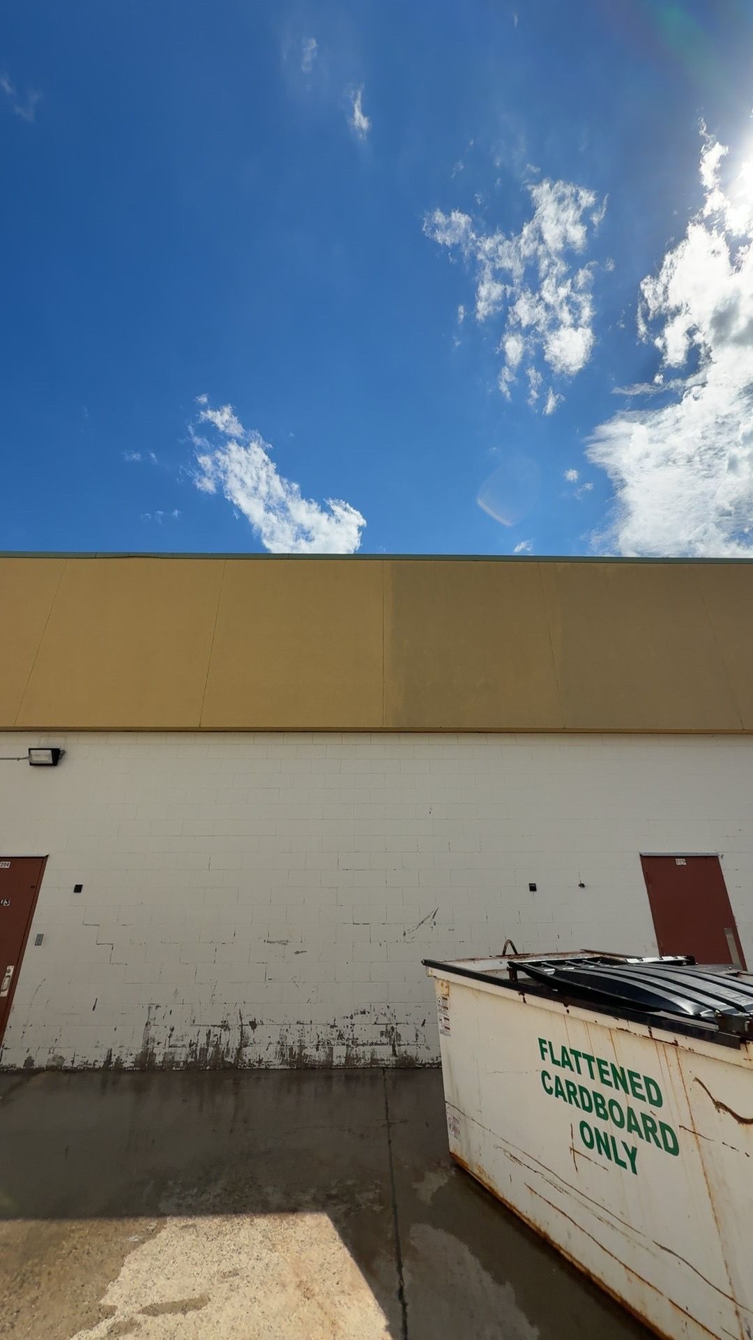 Industrial rooftop with three large dumpsters, red doors, and a cloudy sky.