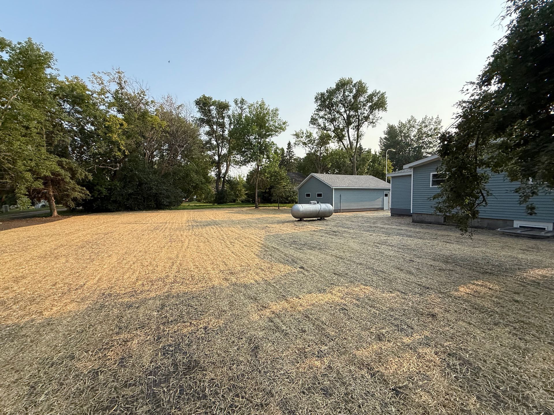 Mowed grassy field with striped lines beside a white fence, under a clear blue sky, near a playground.