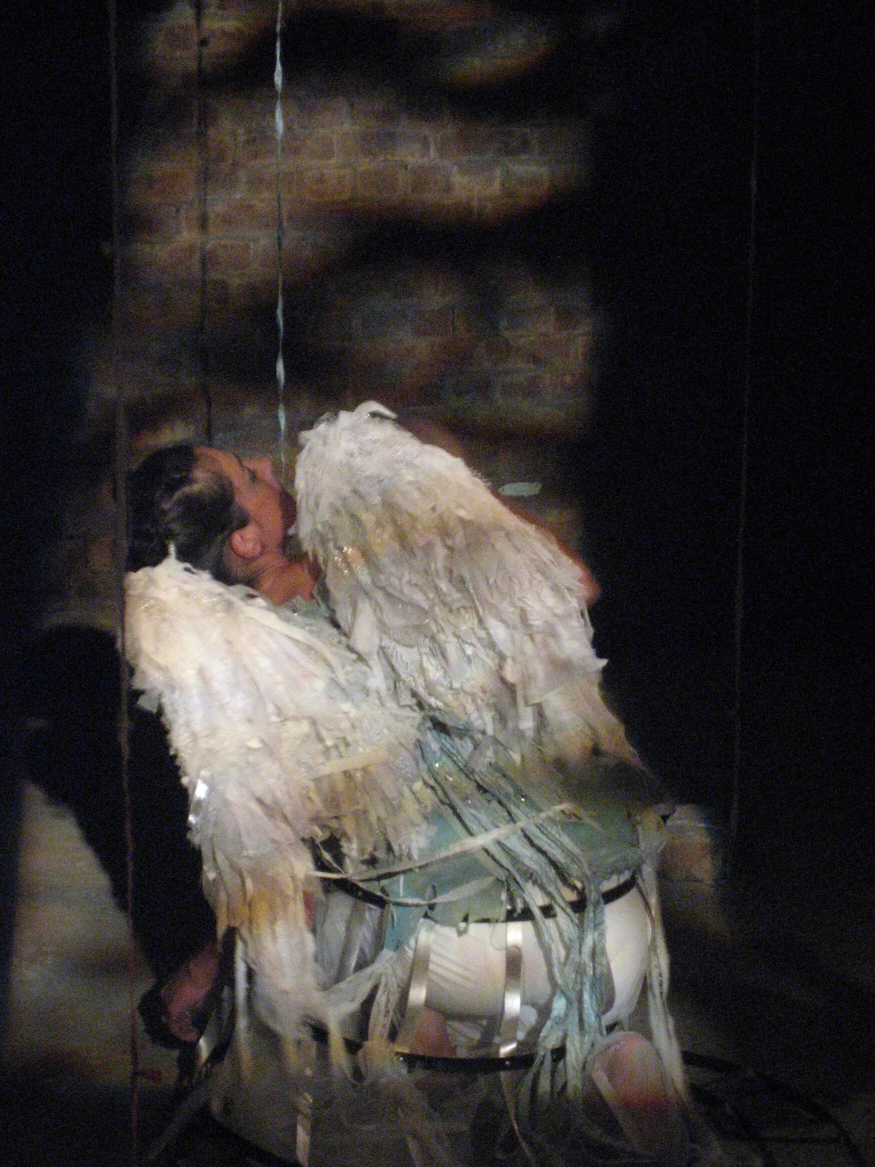Person in a white feathered costume bending forward on a dark stage