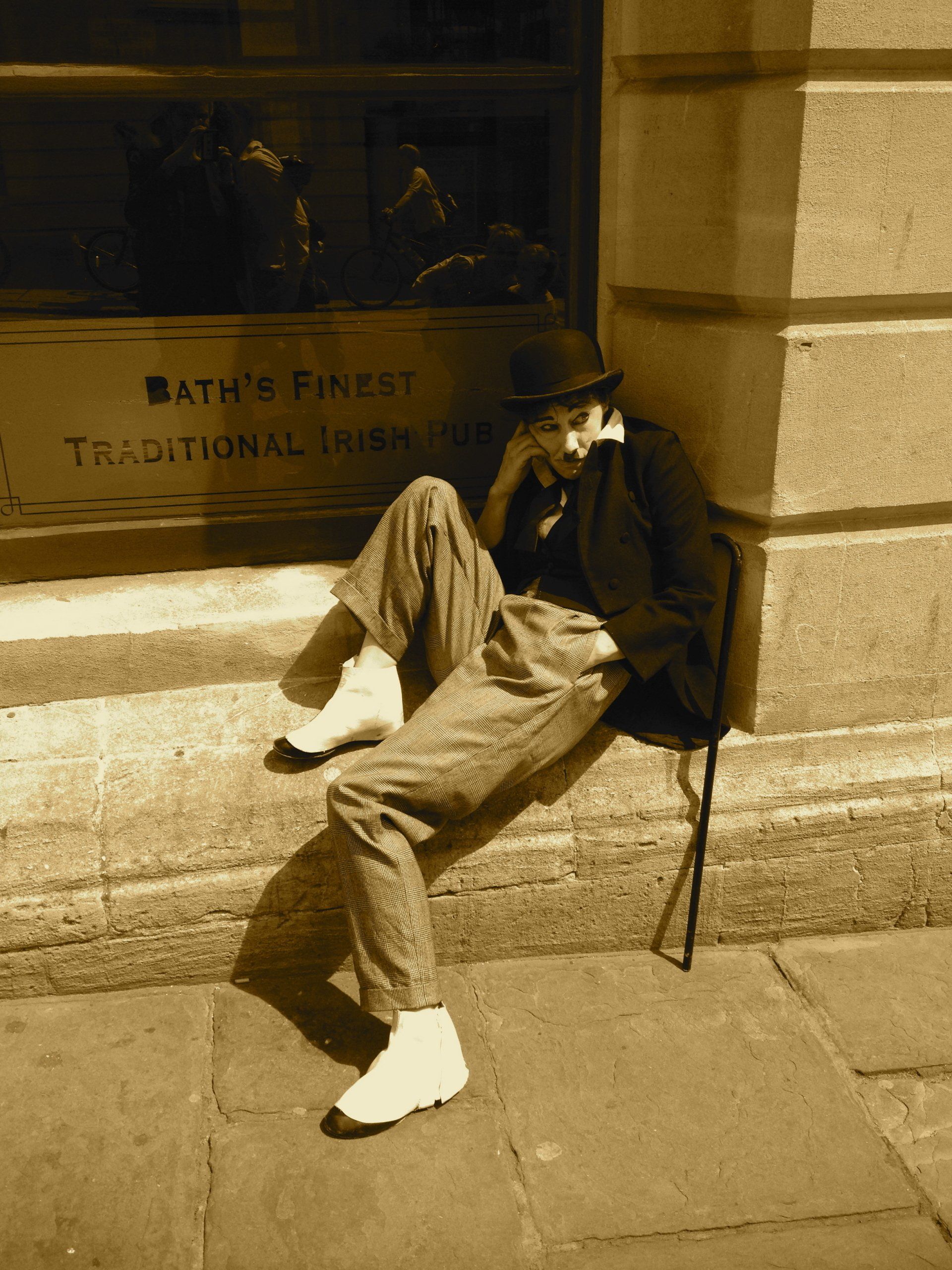Person sitting on stone steps beside a wall, in warm sepia tones, wearing a hat and coat.